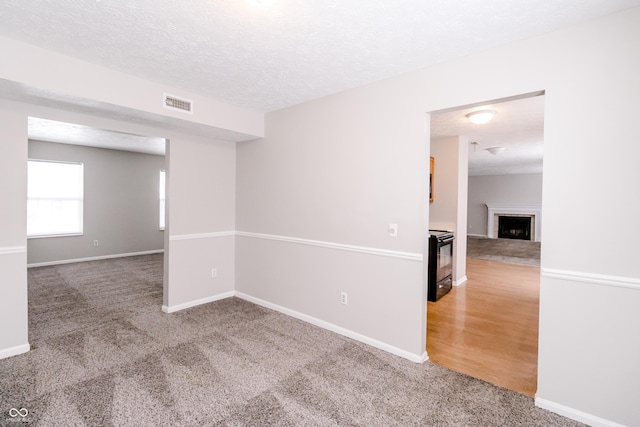 unfurnished room with baseboards, visible vents, a textured ceiling, carpet flooring, and a fireplace