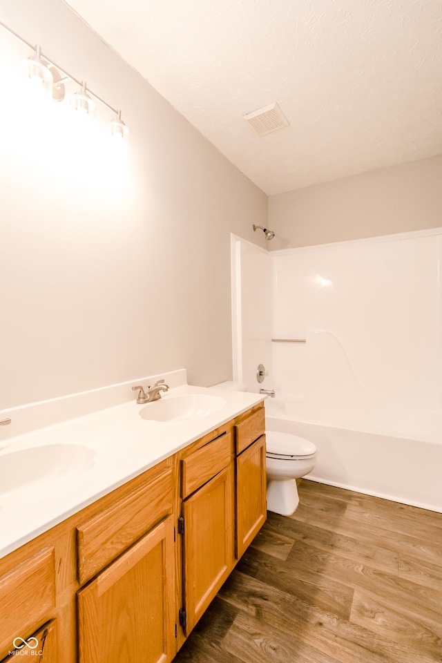 bathroom with toilet, double vanity, a sink, and wood finished floors