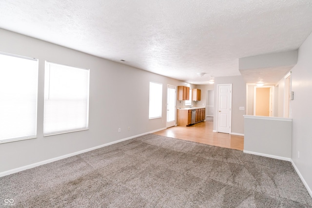 unfurnished living room with light carpet, a textured ceiling, and baseboards