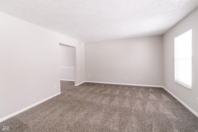 empty room featuring a textured ceiling, carpet flooring, visible vents, and baseboards