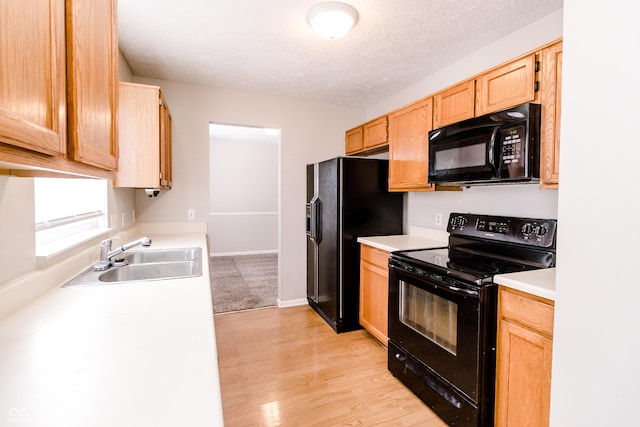 kitchen featuring light countertops, light wood-style flooring, a sink, a textured ceiling, and black appliances