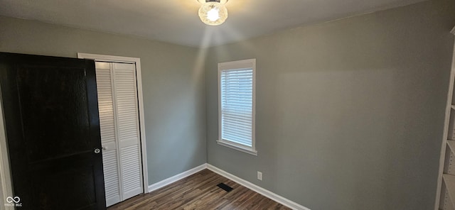 unfurnished bedroom featuring multiple windows, dark wood-type flooring, and a closet