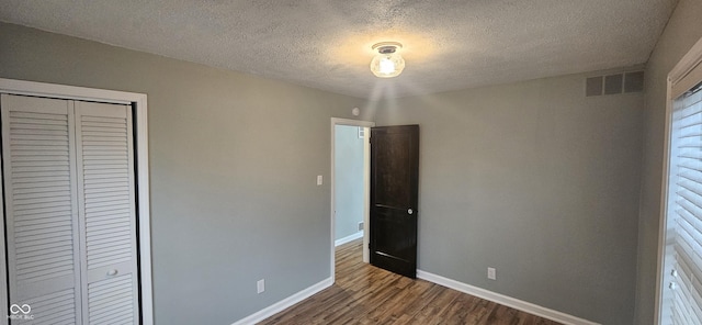 unfurnished bedroom featuring visible vents, a textured ceiling, wood finished floors, a closet, and baseboards