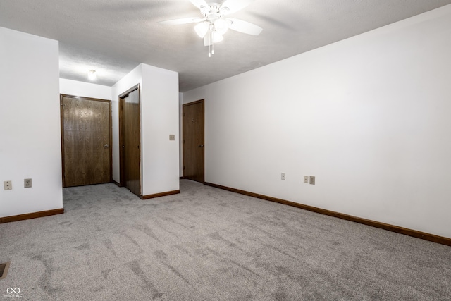 unfurnished bedroom with ceiling fan, a textured ceiling, light colored carpet, baseboards, and multiple closets