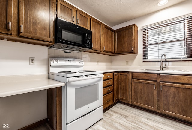 kitchen with white range with electric stovetop, black microwave, light countertops, and a sink