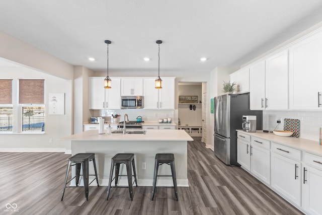 kitchen featuring a kitchen island with sink, hanging light fixtures, stainless steel appliances, and white cabinets