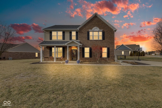 view of front of house with a front yard, covered porch, brick siding, and central AC