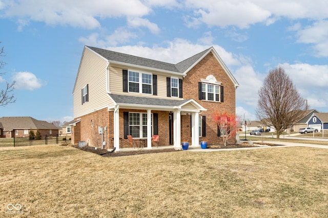 traditional-style home featuring covered porch, brick siding, a front yard, and fence