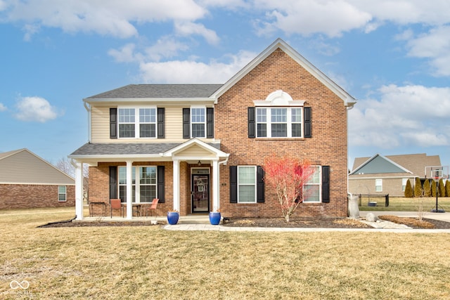 traditional-style house with a shingled roof, covered porch, brick siding, and a front lawn