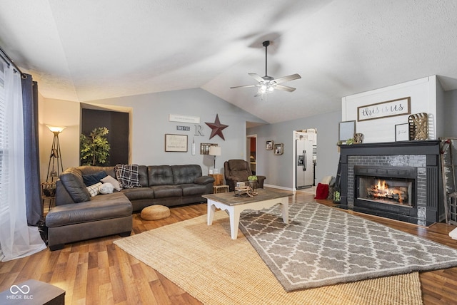 living room with wood-type flooring, vaulted ceiling, a textured ceiling, ceiling fan, and a fireplace