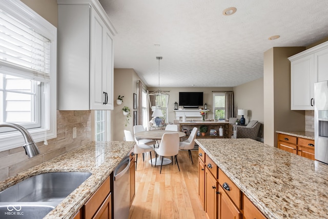 kitchen with sink, white cabinetry, light wood-type flooring, stainless steel appliances, and light stone countertops