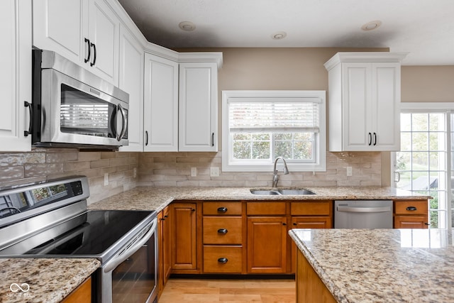 kitchen with appliances with stainless steel finishes, tasteful backsplash, sink, white cabinets, and light stone countertops