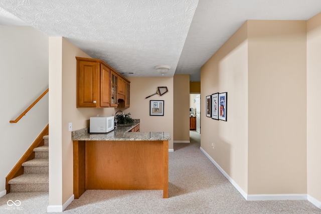 kitchen featuring kitchen peninsula, light carpet, and a textured ceiling