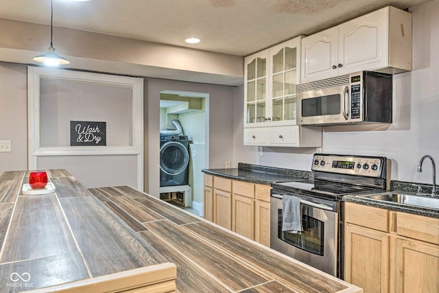 kitchen featuring stainless steel appliances, a sink, washer / clothes dryer, dark countertops, and glass insert cabinets