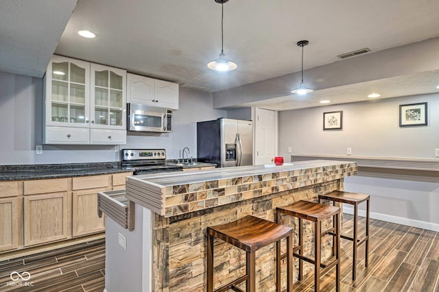 kitchen with visible vents, a kitchen breakfast bar, wood tiled floor, stainless steel appliances, and a sink