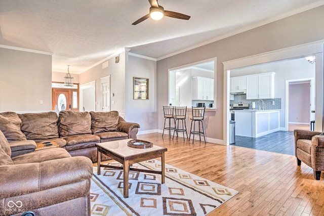 living area with visible vents, a ceiling fan, baseboards, ornamental molding, and light wood-type flooring