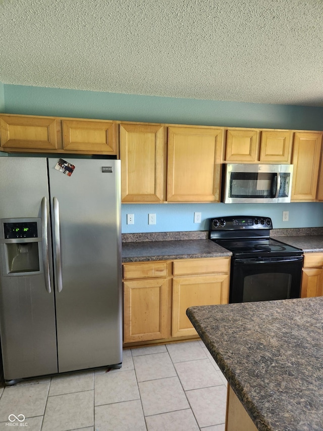 kitchen with appliances with stainless steel finishes, dark countertops, a textured ceiling, light tile patterned floors, and light brown cabinets