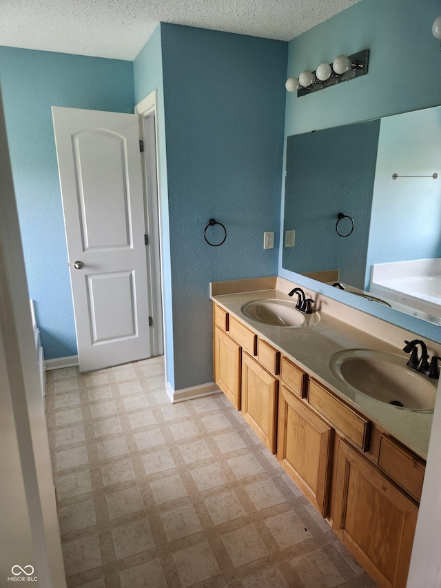 bathroom with tile patterned floors, a garden tub, double vanity, a textured ceiling, and baseboards