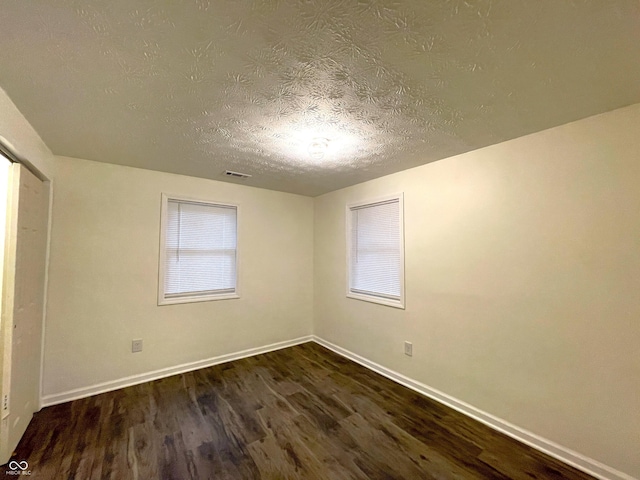 unfurnished room featuring a healthy amount of sunlight, a textured ceiling, and dark hardwood / wood-style flooring