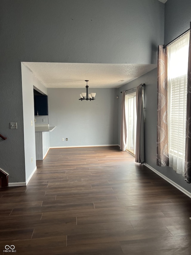 empty room featuring dark wood-type flooring, a chandelier, and a textured ceiling