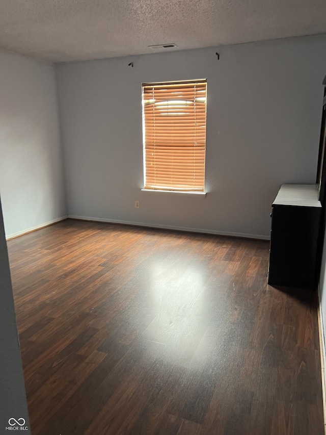 empty room with dark hardwood / wood-style floors and a textured ceiling