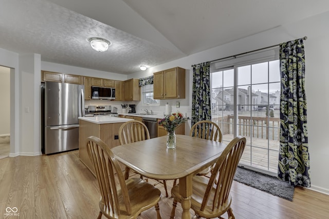 dining room with vaulted ceiling, sink, light hardwood / wood-style floors, and a textured ceiling