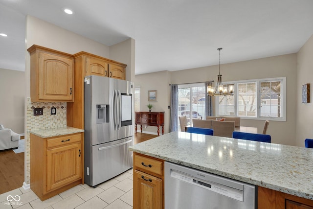 kitchen featuring appliances with stainless steel finishes, an inviting chandelier, light stone counters, decorative backsplash, and decorative light fixtures