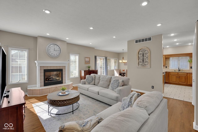 living room featuring a tiled fireplace, sink, and light wood-type flooring