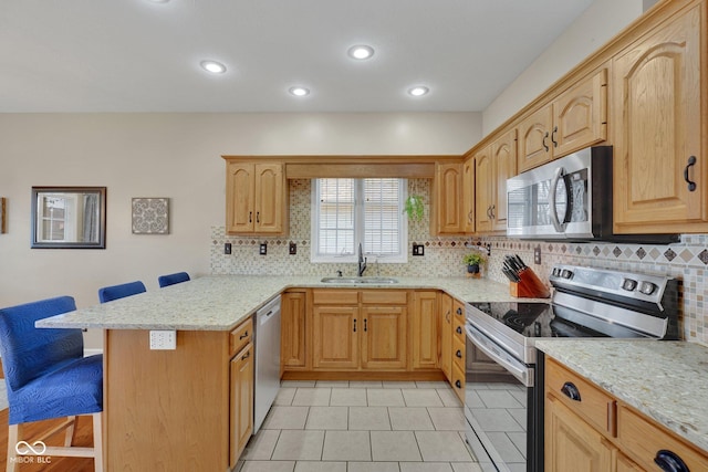 kitchen featuring sink, appliances with stainless steel finishes, light stone counters, a kitchen bar, and decorative backsplash