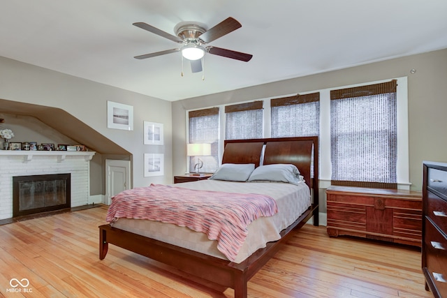 bedroom featuring ceiling fan, a brick fireplace, and light hardwood / wood-style floors