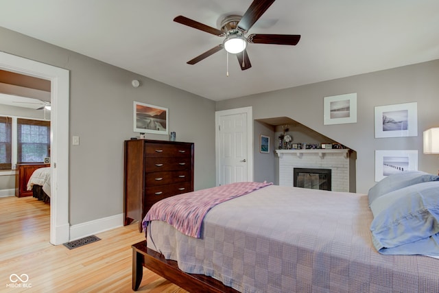 bedroom with a fireplace, light hardwood / wood-style flooring, and ceiling fan