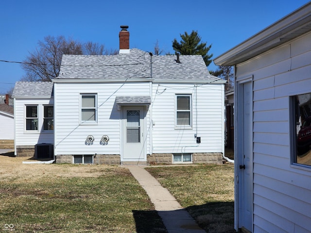 rear view of house featuring a yard, a chimney, central AC, and a shingled roof