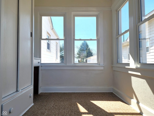 spare room with baseboards and dark colored carpet