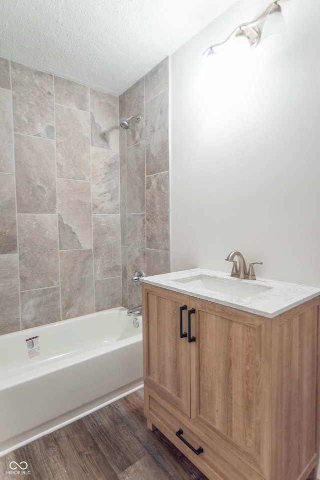 full bathroom with a textured ceiling, shower / washtub combination, wood finished floors, and a sink