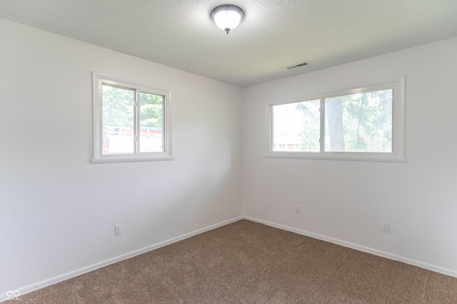 carpeted empty room with baseboards, visible vents, and a textured ceiling