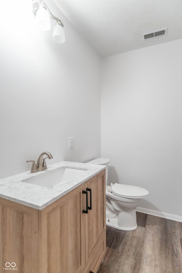 bathroom with vanity, wood finished floors, visible vents, a textured ceiling, and toilet