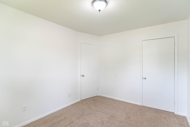 unfurnished bedroom with a textured ceiling, baseboards, and light carpet