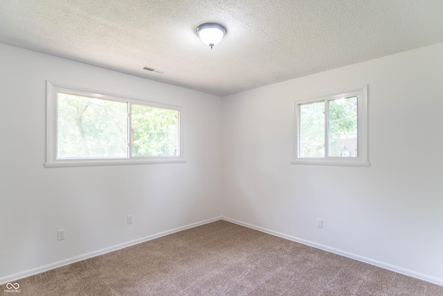 carpeted empty room featuring visible vents, a textured ceiling, and baseboards