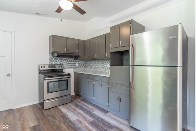 kitchen with gray cabinetry, under cabinet range hood, appliances with stainless steel finishes, decorative backsplash, and dark wood-style flooring