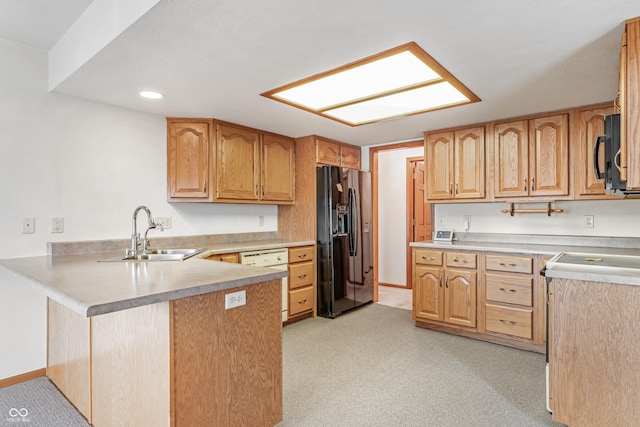 kitchen featuring a peninsula, black appliances, light countertops, and a sink