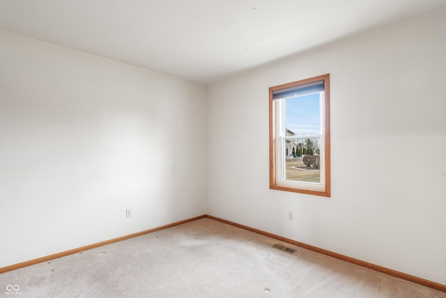 empty room with baseboards, visible vents, and light colored carpet