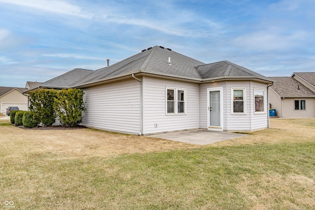 rear view of property with a shingled roof, a patio area, and a lawn