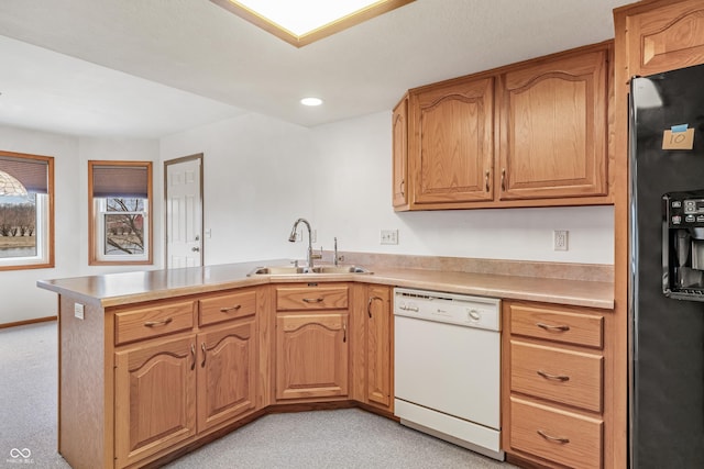 kitchen with dishwasher, a peninsula, black refrigerator with ice dispenser, light countertops, and a sink