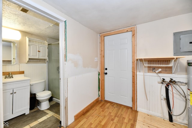 bathroom with a shower with shower door, hardwood / wood-style flooring, vanity, electric panel, and toilet