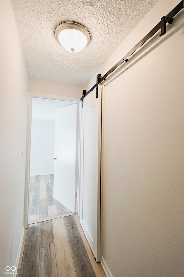 hallway featuring light hardwood / wood-style flooring, a barn door, and a textured ceiling