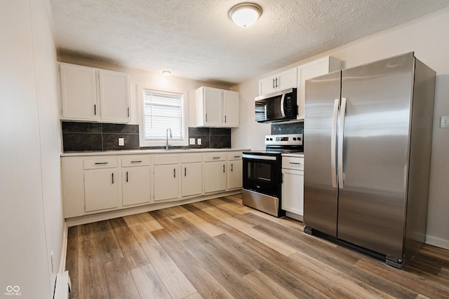 kitchen with appliances with stainless steel finishes, sink, backsplash, light hardwood / wood-style flooring, and white cabinets