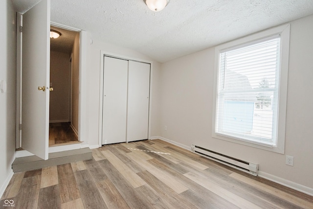 unfurnished bedroom featuring a baseboard radiator, a closet, a textured ceiling, vaulted ceiling, and light wood-type flooring