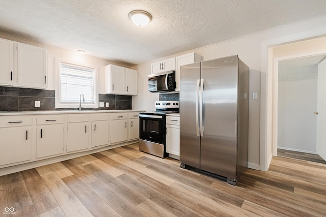 kitchen with appliances with stainless steel finishes, tasteful backsplash, light hardwood / wood-style floors, sink, and white cabinetry