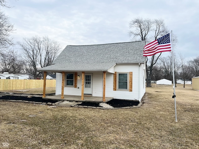 view of front of house with a shingled roof, a porch, a front yard, and fence