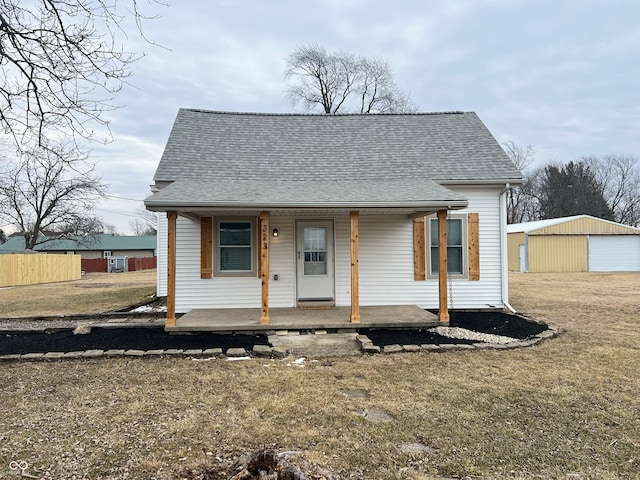 bungalow-style house with an outbuilding, roof with shingles, a porch, a front yard, and fence